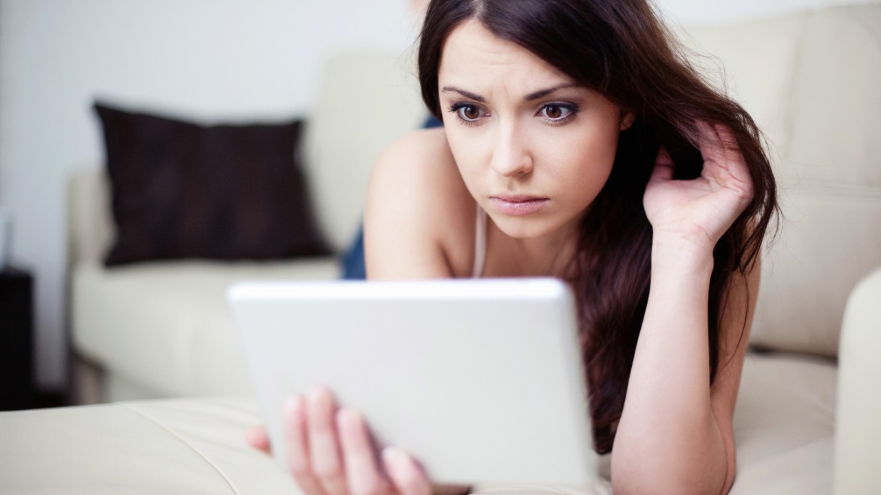 Sad woman lying on couch with tablet